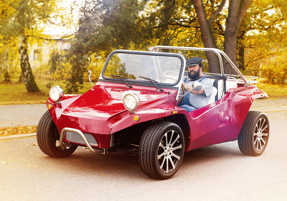 Man driving a bright red dune buggy with an open top along a tree lined autumn street